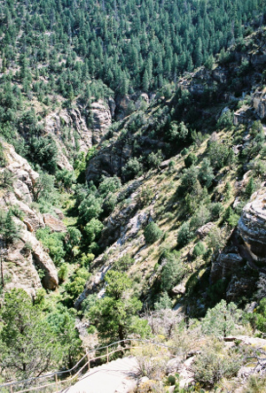 [View looks down into the currently waterless gorge. The sides of the canyon are steep on both the right and the left. Many trees cover the hillside. A paved walkway with a metal railing is at the bottom edge of the image.]